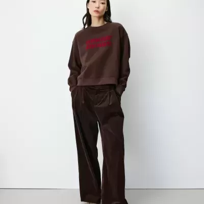 Mulher com sweat castanha com texto vermelho e calças largas de veludo castanhas