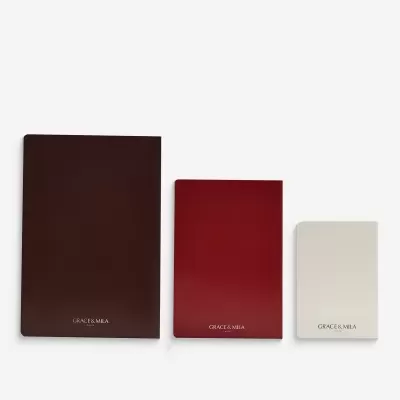 Três agendas de capa lisa em castanho escuro, vermelho e bege com texto GRACE & MILA PARIS