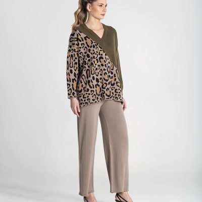 Mulher com camisola estampada leopardo e verde-oliva, calças bége largas e sapatos pretos de salto, fundo branco