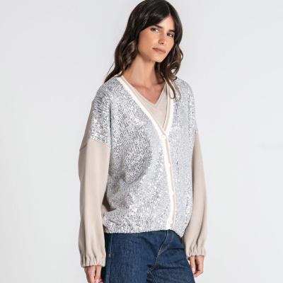 Cardigan bege com painel frontal prateado de lantejoulas e botões brancos, calças de ganga azuis.