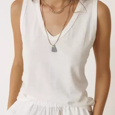 Mulher com camisola sem mangas branca, calças brancas com renda, colares coloridos com pendentes.