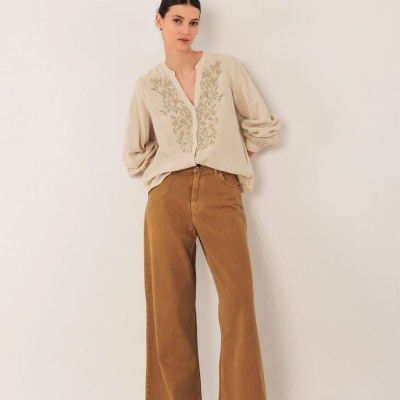 Mulher vestindo blusa bege bordada e calças largas castanhas com sapatos castanhos escuros
