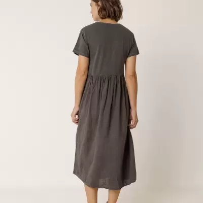 Vestido cinzento escuro com manga curta visto de costas, mulher usa ténis brancos, fundo branco