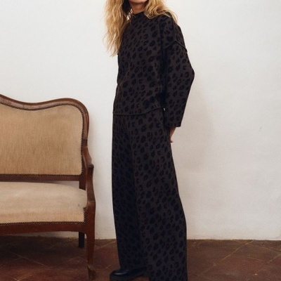 Conjunto preto com padrão animal print, mulher com sapatos pretos, cadeira antiga bege e chão em azulejo