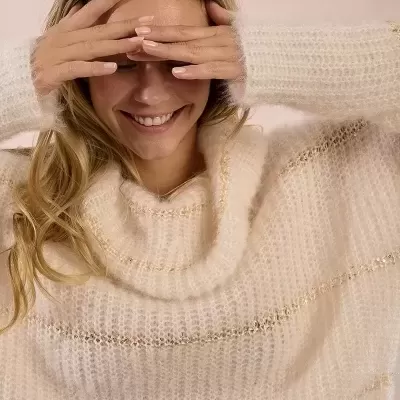 Camisola felpuda branca com riscas douradas usada por mulher sorridente