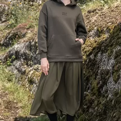 Mulher com hoodie verde-oliva e boné bege ao ar livre em ambiente natural