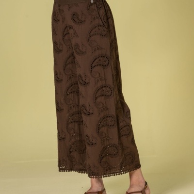 Saia comprida castanha bordada com padrão paisley e pompons na barra, com sandálias castanhas.