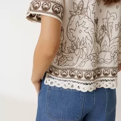 Blusa branca de manga curta com bordados castanhos e calções de ganga azuis