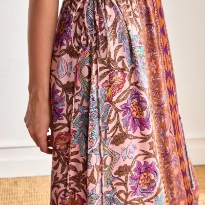 Vestido longo floral colorido com cordão na cintura, mulher ao lado, fundo claro e tapete de fibra natural