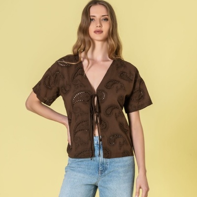 Blusa castanha de manga curta com padrão recortado e laços frontais, combinada com jeans claros