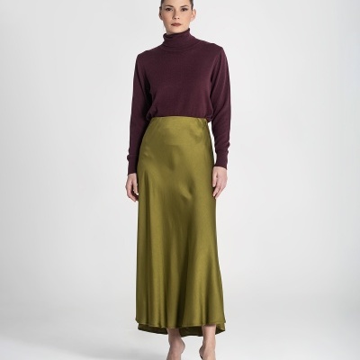 Mulher com camisola castanha e saia verde oliva em fundo branco.