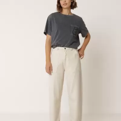 Mulher com t-shirt preta, calças brancas largas e mocassins bejes