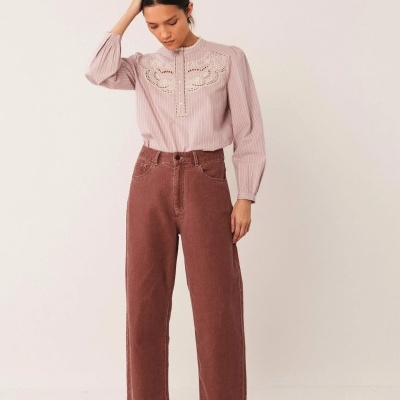 Mulher a vestir blusa cor de rosa clara com bordados e calças castanhas largas