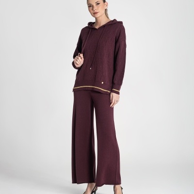 Mulher vestindo conjunto hoodie e calças largas bordô com detalhes dourados e saltos pretos.