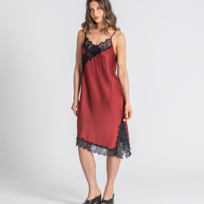 Mulher a usar vestido vermelho com renda preta e sandálias pretas em fundo branco.