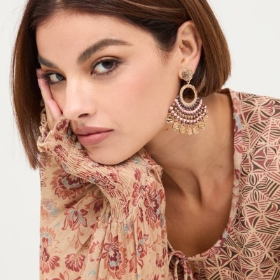 Brincos pendentes decorados com contas e pingentes usados por mulher com blusa floral