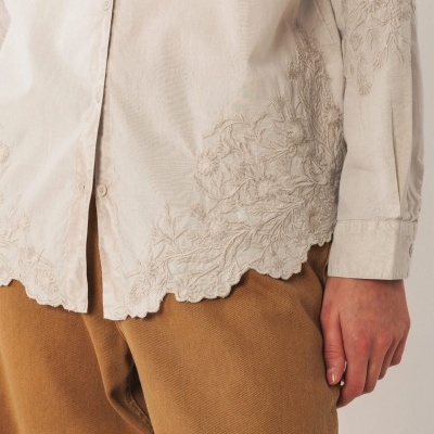 Camisa creme com bordados florais e calças castanhas de veludo cotelê.