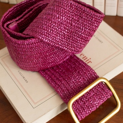 Cinto trançado magenta com fivela dourada sobre livros