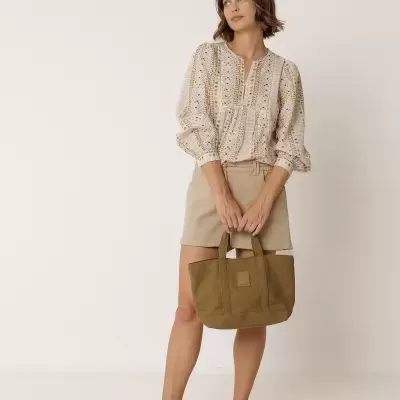 Mulher com blusa bege estampada, saia bege, e mala tote castanha