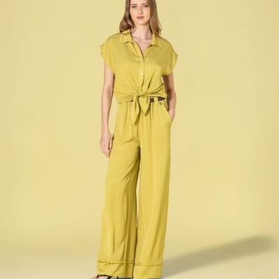 Mulher com conjunto amarelo de camisa curta com nó e calças largas, sandálias pretas, fundo bege