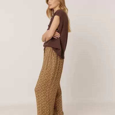 Mulher com camisola castanha sem mangas e calças largas mostarda com padrão branco
