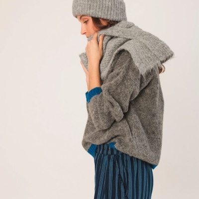 Mulher com gorro e camisola cinza de malha, calças azul com riscas