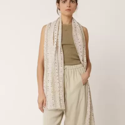 Mulher com cachecol bege com padrão geométrico e roupa clara em fundo neutro