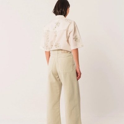 Mulher de costas com camisa branca estampada e calças largas bege