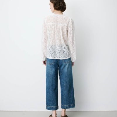 Pessoa de costas com blusa branca de renda, jeans azuis e sapatos castanhos
