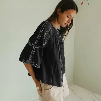 Mulher com blusa preta bordada e calção bege em ambiente interior