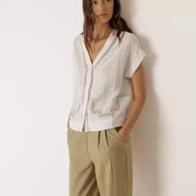 Mulher com camisa branca de manga curta com renda e calças bege riscada