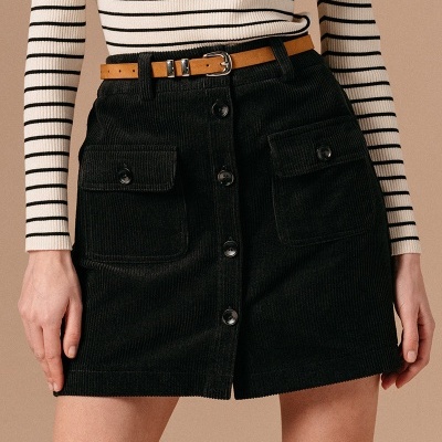 Saia curta preta de veludo com botões frontais e bolsos, cinto castanho e camisola de riscas pretas e brancas.