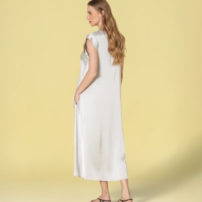 Mulher de costas com vestido comprido branco e sandálias pretas em fundo amarelo