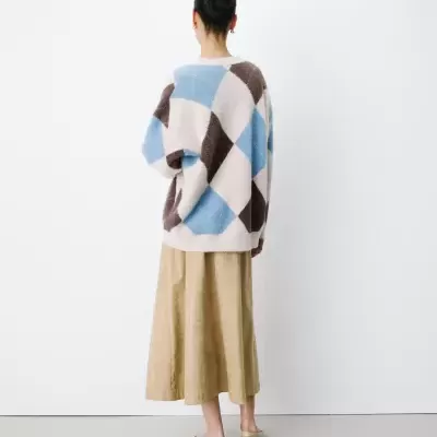 Pessoa de costas com camisola padrão geométrico azul, bege e castanho, saia bege e sapatos baixos cor de pele.