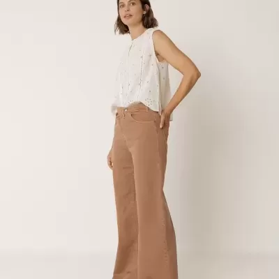 Mulher com blusa branca de algodão bordada e calças largas castanhas em fundo branco