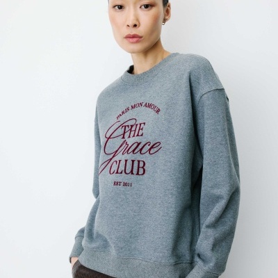 Sweatshirt cinzenta com texto bordado e mulher com calças castanhas