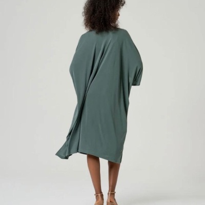 Vestido verde-acinzentado solto visto por trás com sandálias de salto castanhas.