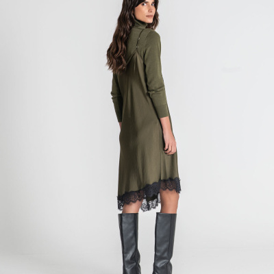 Mulher vista de costas com vestido midi verde com renda preta e botas altas pretas.