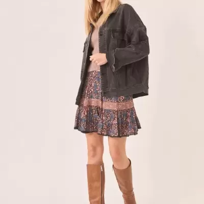Mulher com casaco denim preto, saia floral e botas castanhas