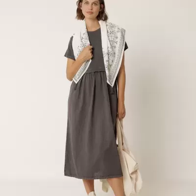 Mulher com vestido midi cinza, lenço branco bordado, ténis brancos e bolsa bege