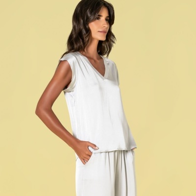 Mulher vestindo camisola branca sem mangas e calças brancas soltas a fundo bege