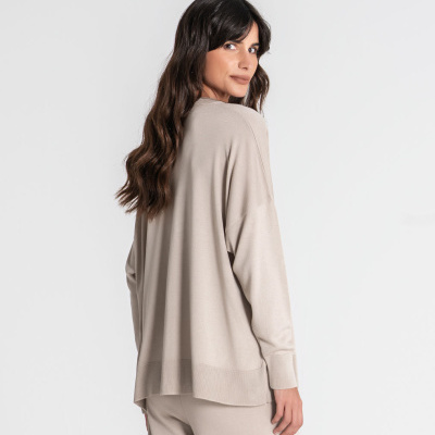 Mulher de costas com fato bege claro, camisola mangas compridas e calças.
