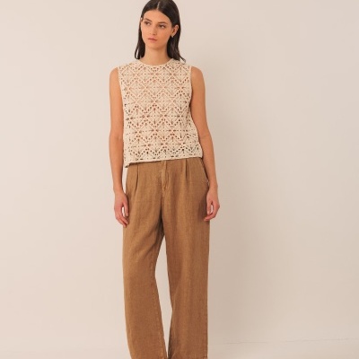mulher com blusa de crochet bege e calças castanhas largas