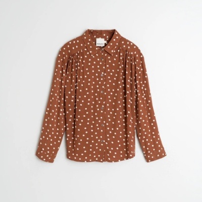 Camisa castanha de bolinhas brancas feminina com botões e gola, pendurada num fundo branco