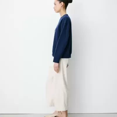 Pessoa de perfil com camisola azul escura, saia branca e sapatos bege
