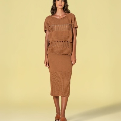 Mulher vestida com conjunto castanho de malha e sandálias castanhas sobre fundo amarelo claro