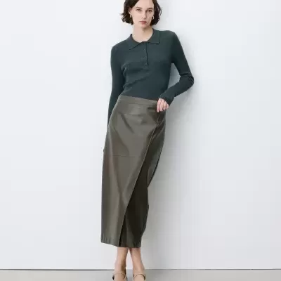 Mulher com camisola cinza escuro de malha e saia midi verde de couro sintético