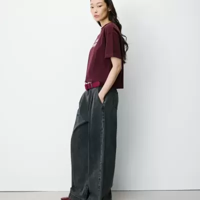 Mulher de perfil com t-shirt vinho e calças largas cinza