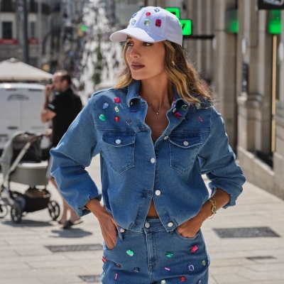 Mulher com casaco e calções de ganga com pedras coloridas e boné branco com pedras