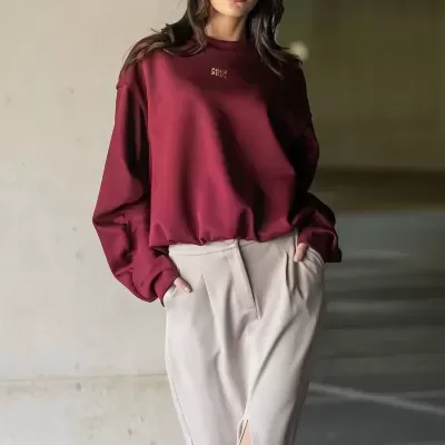 Mulher com casaco vinho 'FOUR SOULS', boné de veludo cotelê vinho e saia bege com fenda.